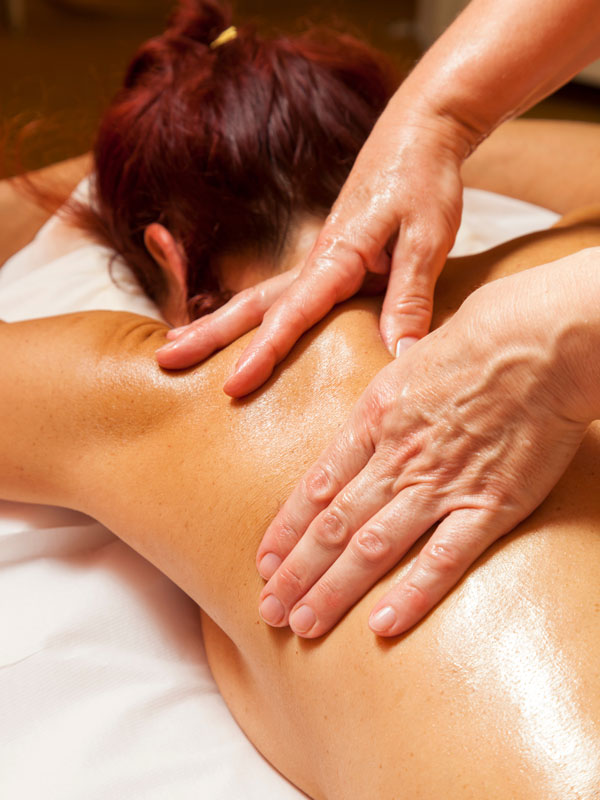 Frau erhält eine wohltuende Massage im Schulterbereich und oberen Rücken auf einer Behandlungsliege