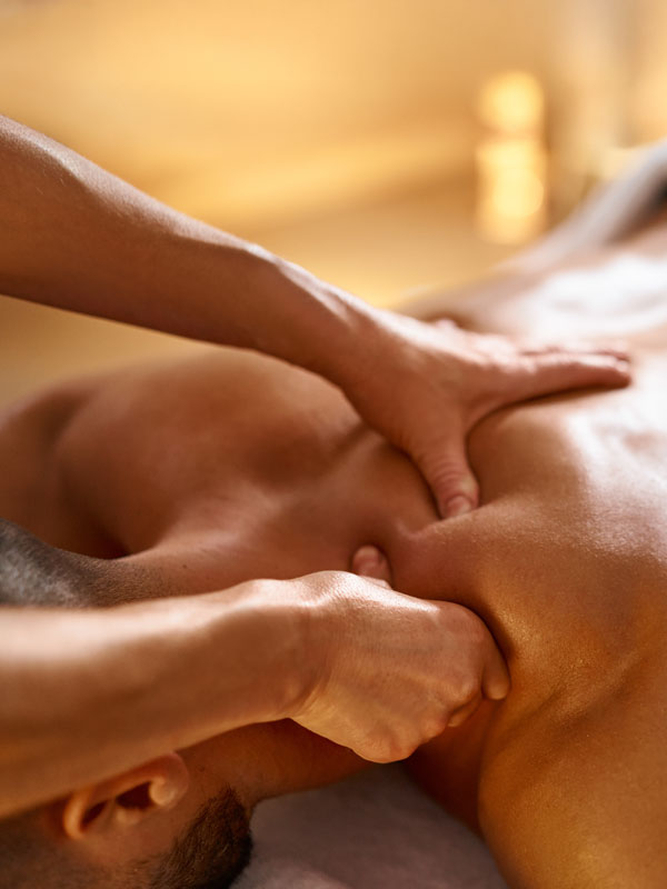 Therapeutische Massage an Nacken und Schultern eines Patienten auf einer Behandlungsliege